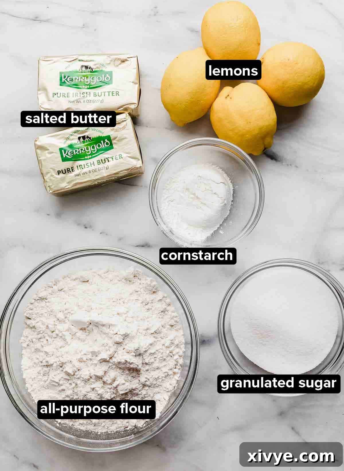 Lemon Shortbread Cookies ingredients portioned into glass bowls on a white and gray marble background: softened butter, all-purpose flour, fresh lemons, cornstarch.