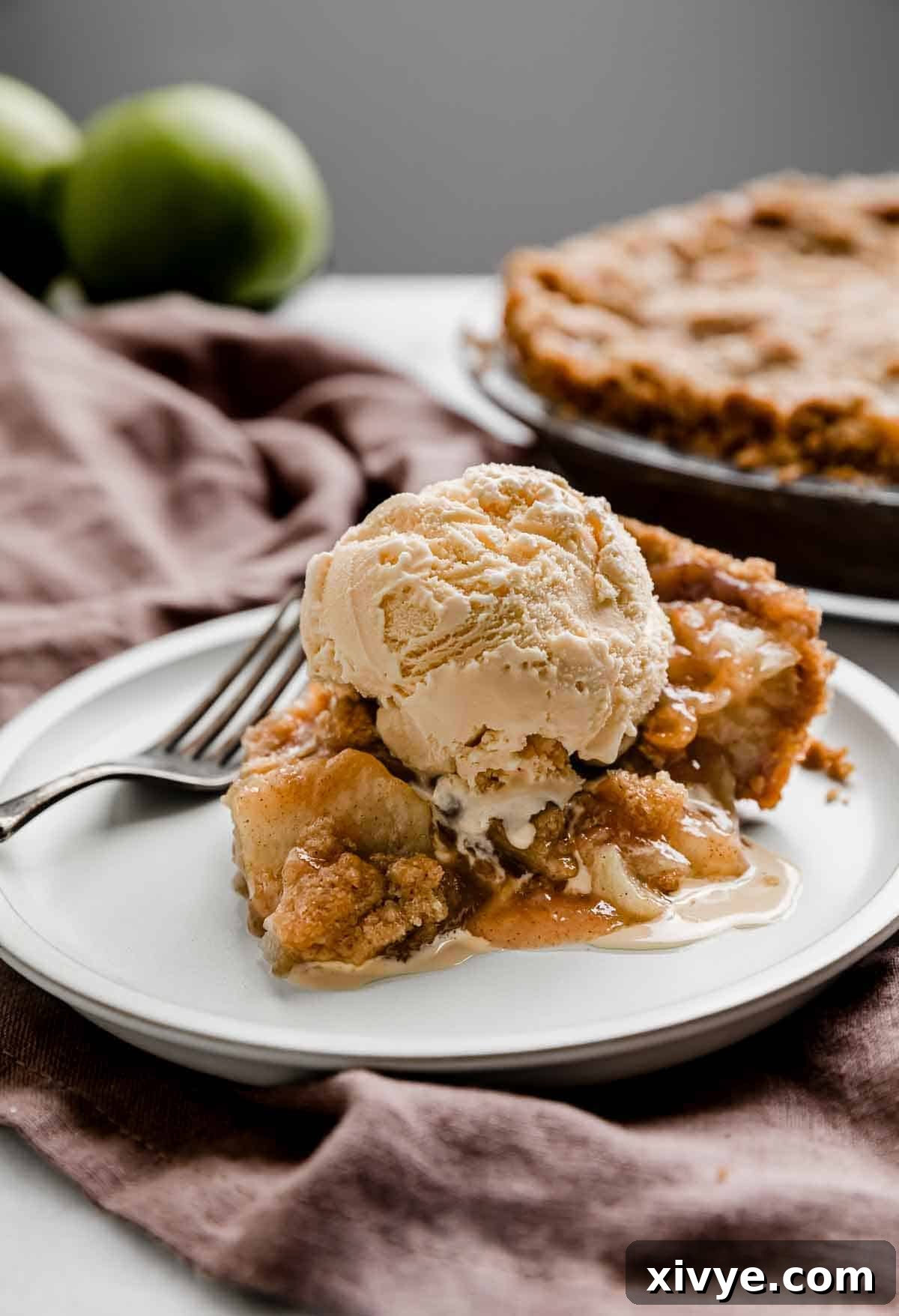 Autumn Apple Pie Graham Cracker Crunch 2 A perfectly baked slice of Apple Pie with Graham Cracker Crust, showing the crisp topping and tender apple filling, served on a white plate with the full pie blurred in the background.