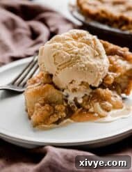 Autumn Apple Pie Graham Cracker Crunch 9 An Apple Pie slice on a white plate topped with a scoop of vanilla ice cream, enticingly presented.