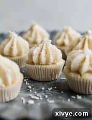 Mini vanilla cupcakes topped with vanilla frosting and white sprinkles, on a metal silver tray.