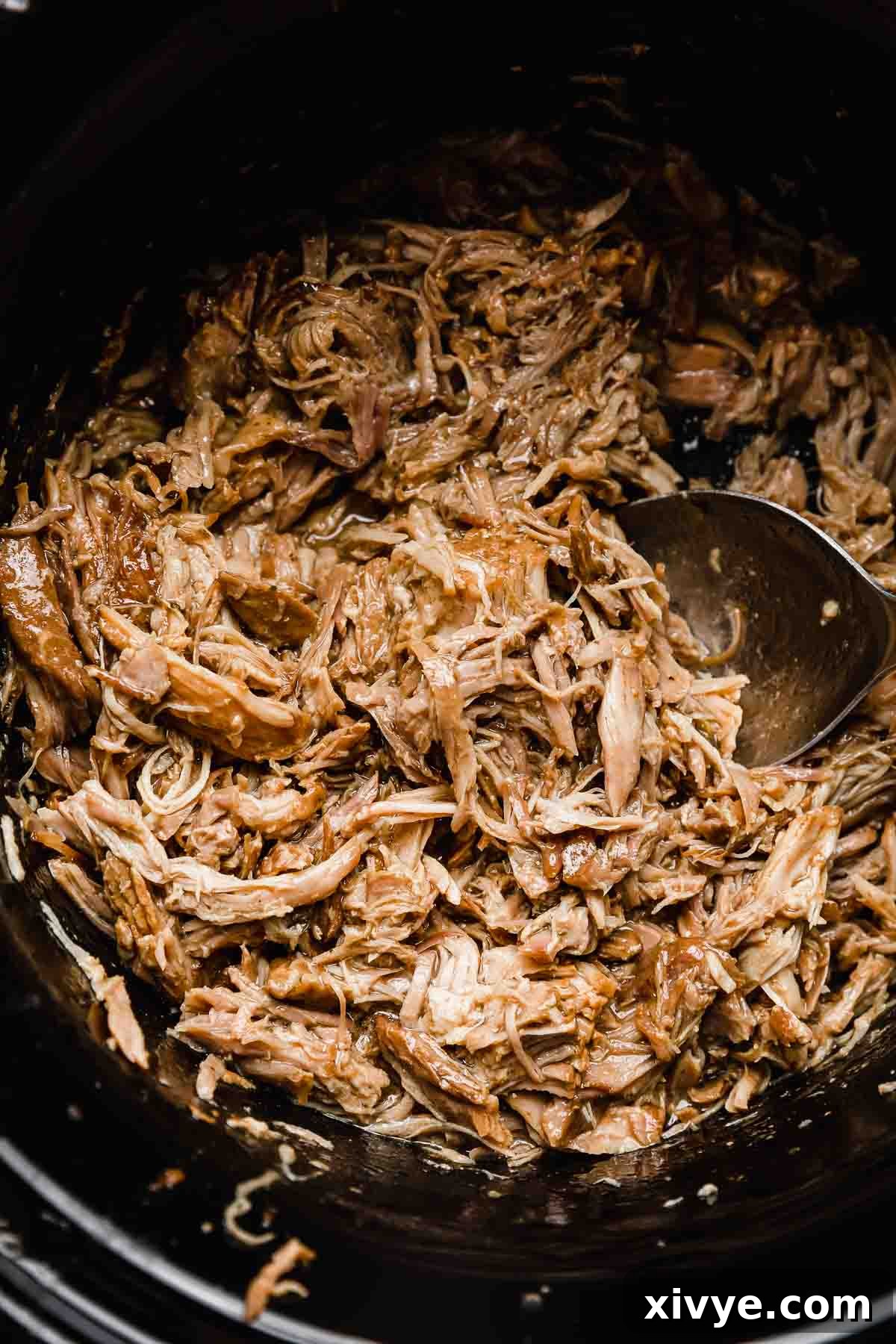 Close up photo of crock pot Mississippi Pork Roast meat in a black slow cooker.
