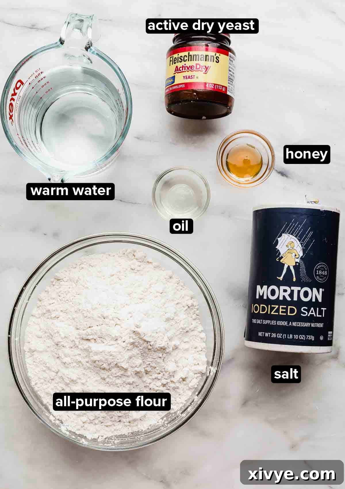 Restaurant Quality Pizza Dough Made Easy at Home 3 Six ingredients for pizza dough laid out on a white background: water, all-purpose flour, sea salt, active dry yeast, olive oil, and honey.