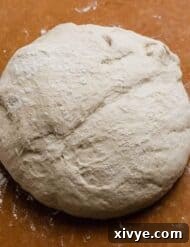 A perfectly formed ball of homemade pizza dough on a brown background.