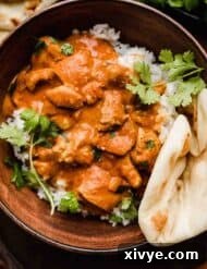 Chicken Tikka Masala in a brown bowl garnished with cilantro and a side of naan bread.