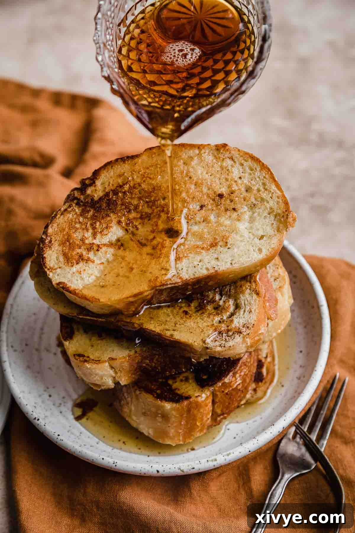 Artisan French Toast 2 Golden French Bread French Toast slices generously drizzled with warm maple syrup, served on a white plate, ready for breakfast or brunch.