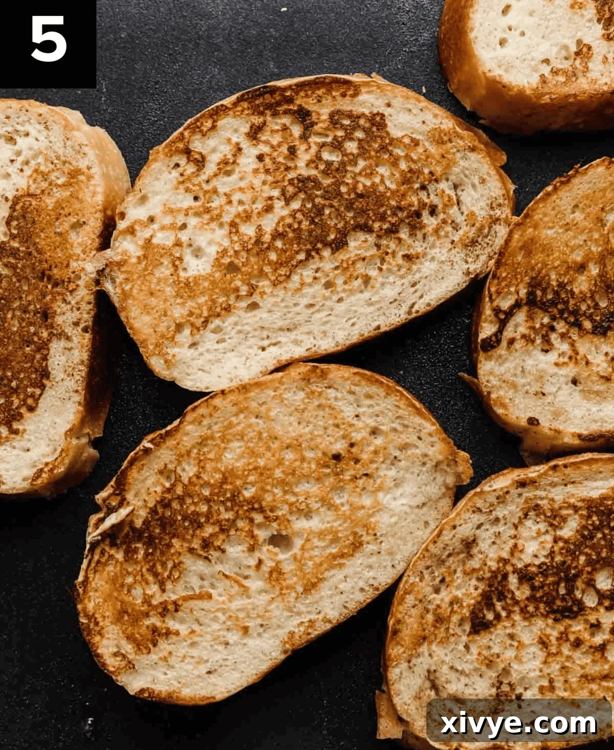 Artisan French Toast 5 Freshly cooked French Bread French Toast slices resting on a black griddle, showcasing their golden-brown perfection.