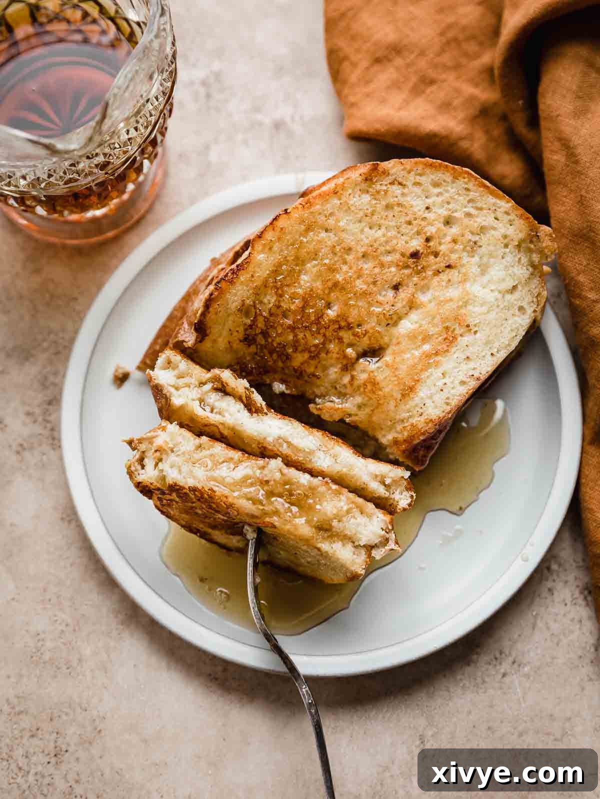 Artisan French Toast 7 A slice of golden French Bread French Toast on a white plate, with a fork gently cutting into it, ready to be enjoyed.