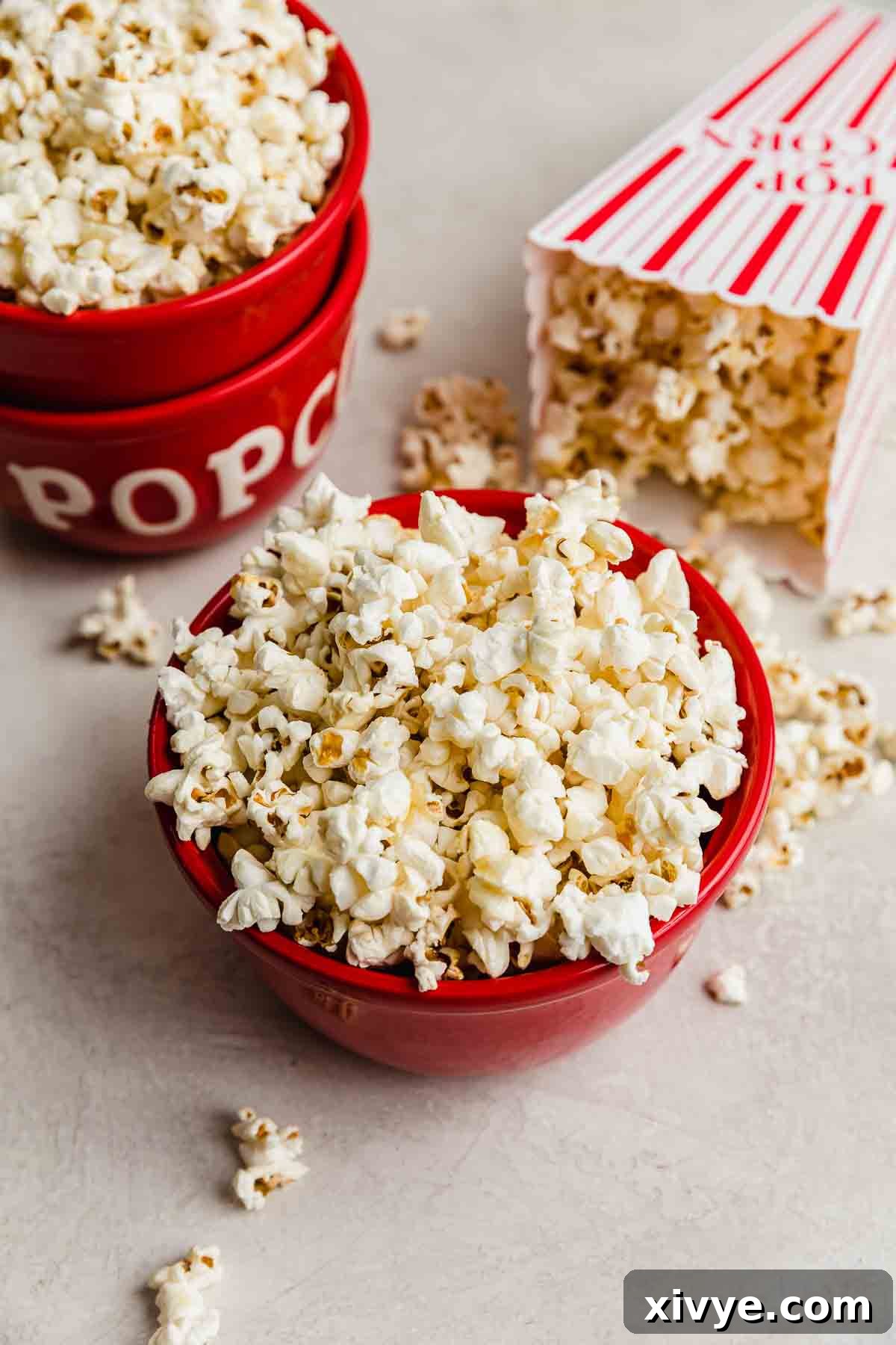 Sweet and Salty Kettle Corn 2 Kettle Corn Popcorn in a vibrant red bowl on a light gray background, with additional kettle corn pieces scattered around the bowl.