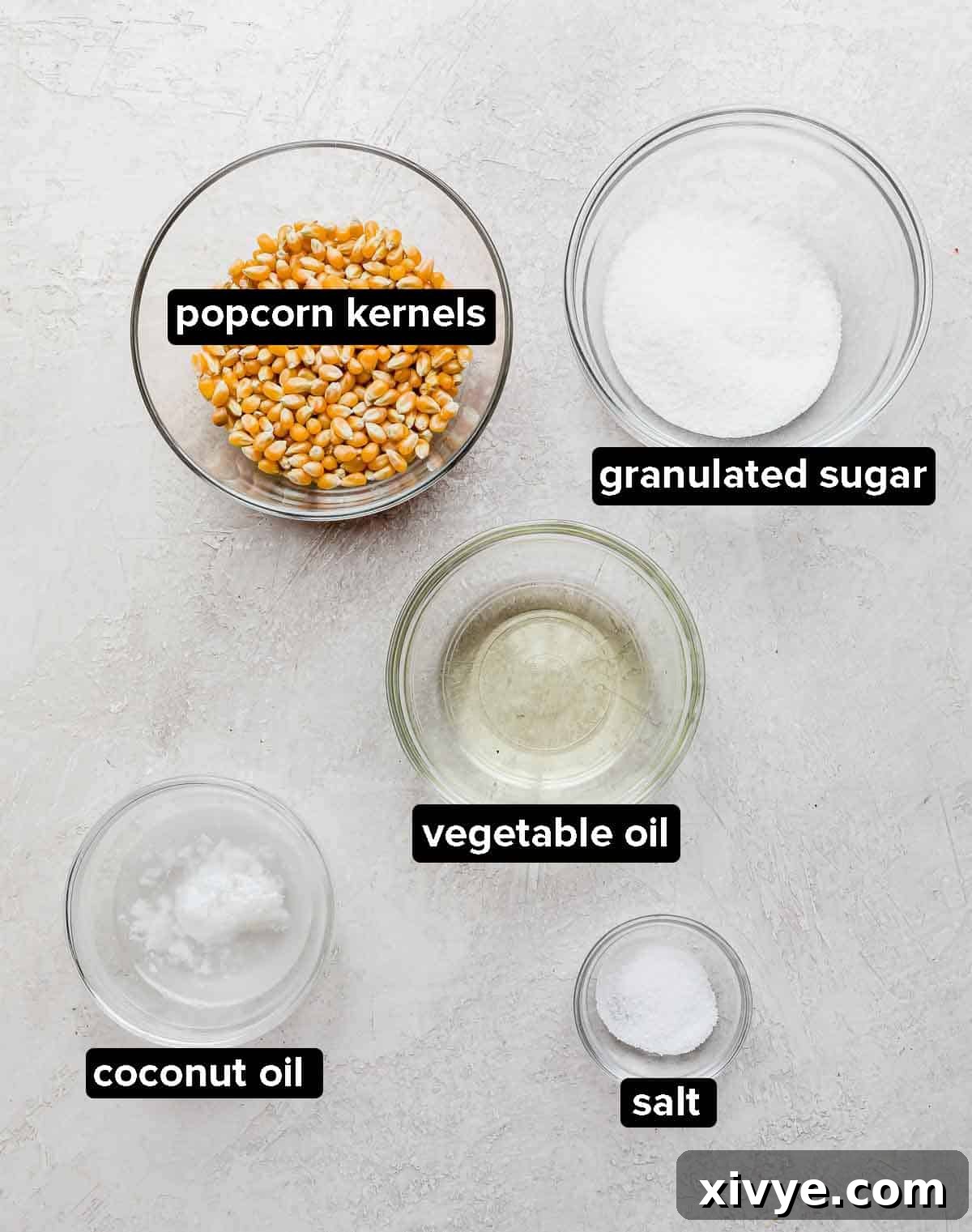 Sweet and Salty Kettle Corn 3 Kettle Corn Popcorn ingredients displayed on a light gray textured background: vegetable oil, coconut oil, unpopped popcorn kernels, salt, and granulated sugar.