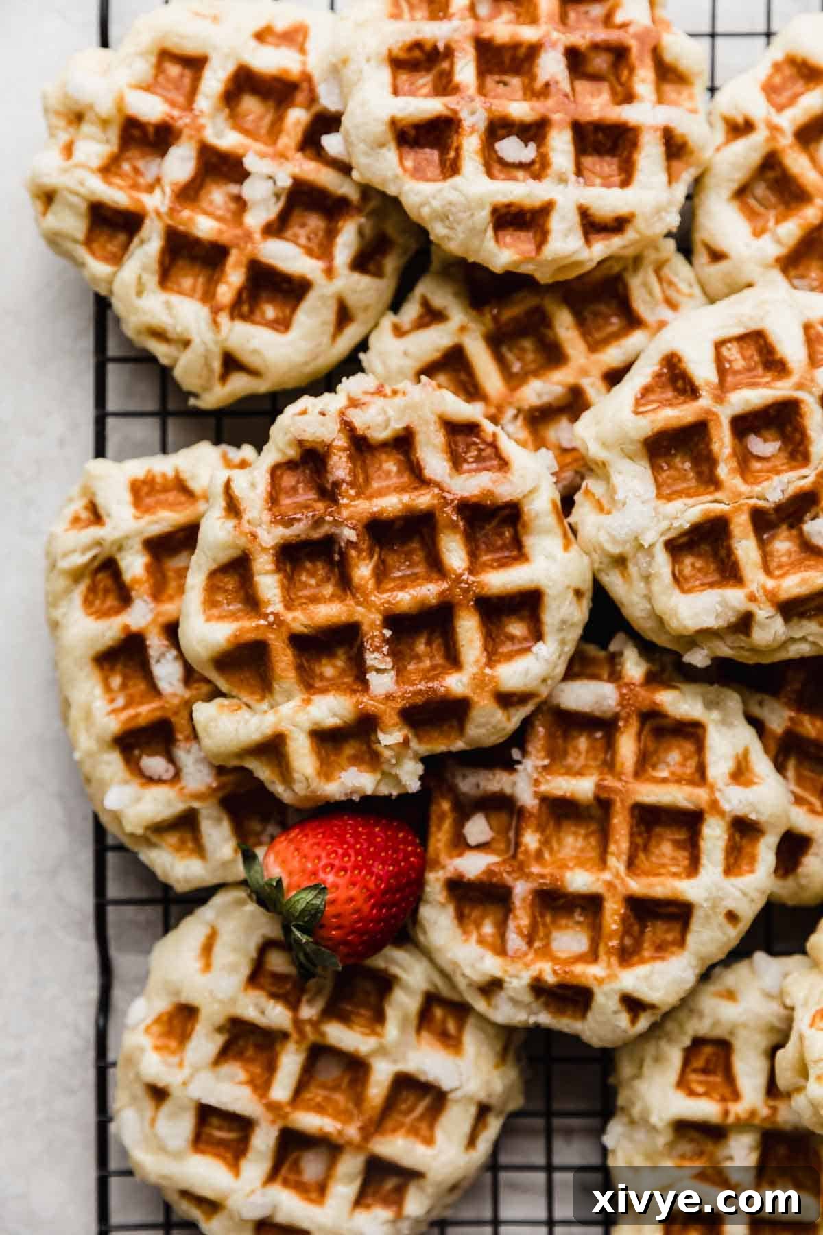 Belgian Liege Waffles stacked on top of one another on a black cooling rack, showcasing their golden-brown exterior and irregular shapes from caramelized pearl sugar.