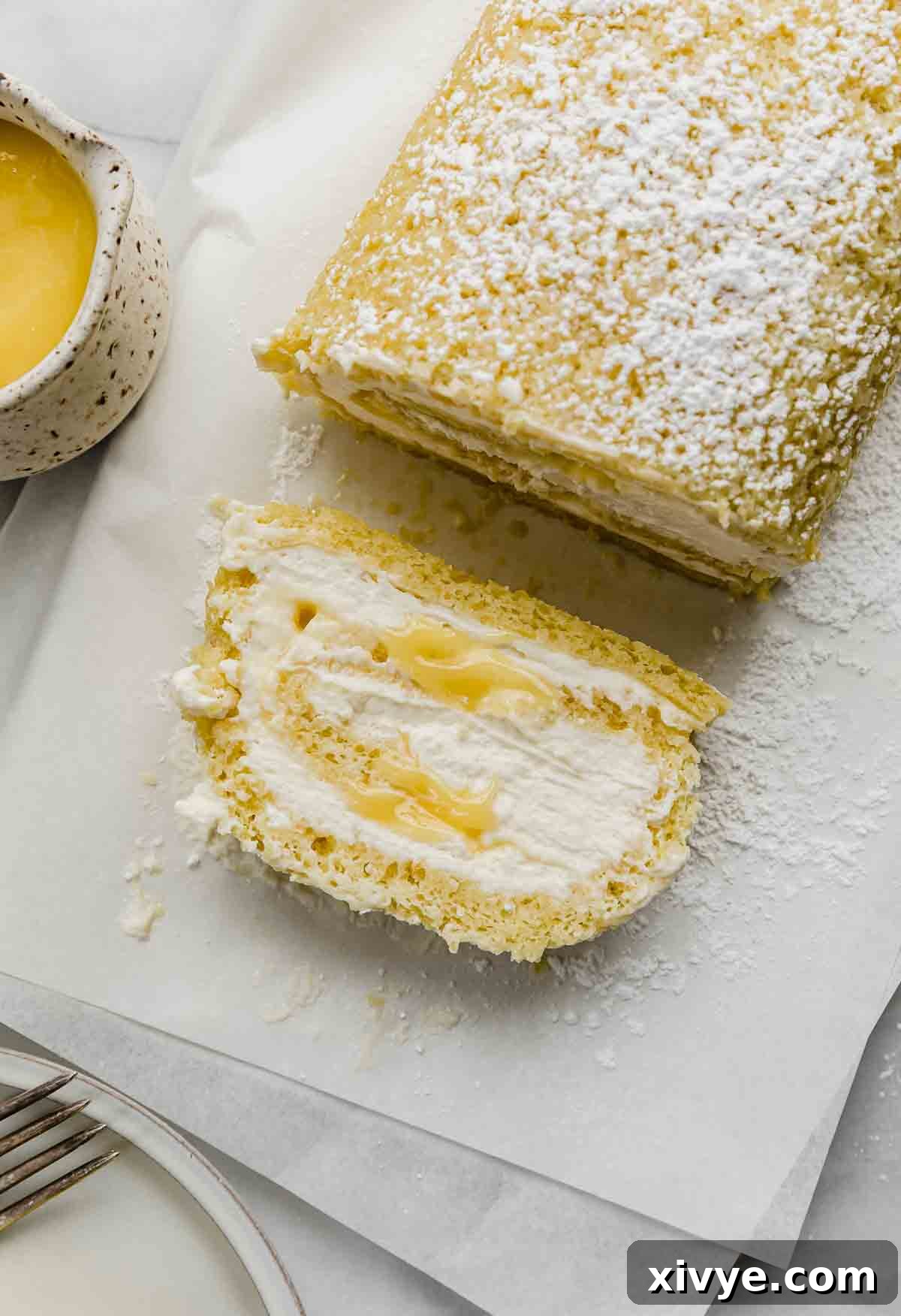 A beautifully presented slice of Lemon Swiss Roll, showcasing its layers of soft sponge, fluffy mascarpone cream, and golden lemon curd, resting on white parchment paper.
