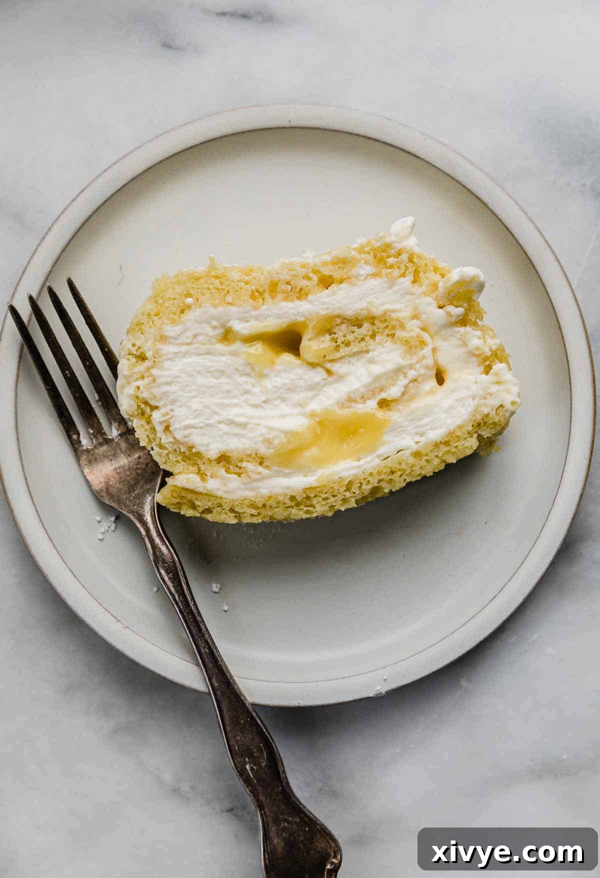 A delectable slice of Lemon Swiss Roll, showcasing the vibrant lemon curd and creamy mascarpone filling, served on a pristine white plate with an elegant fork beside it.