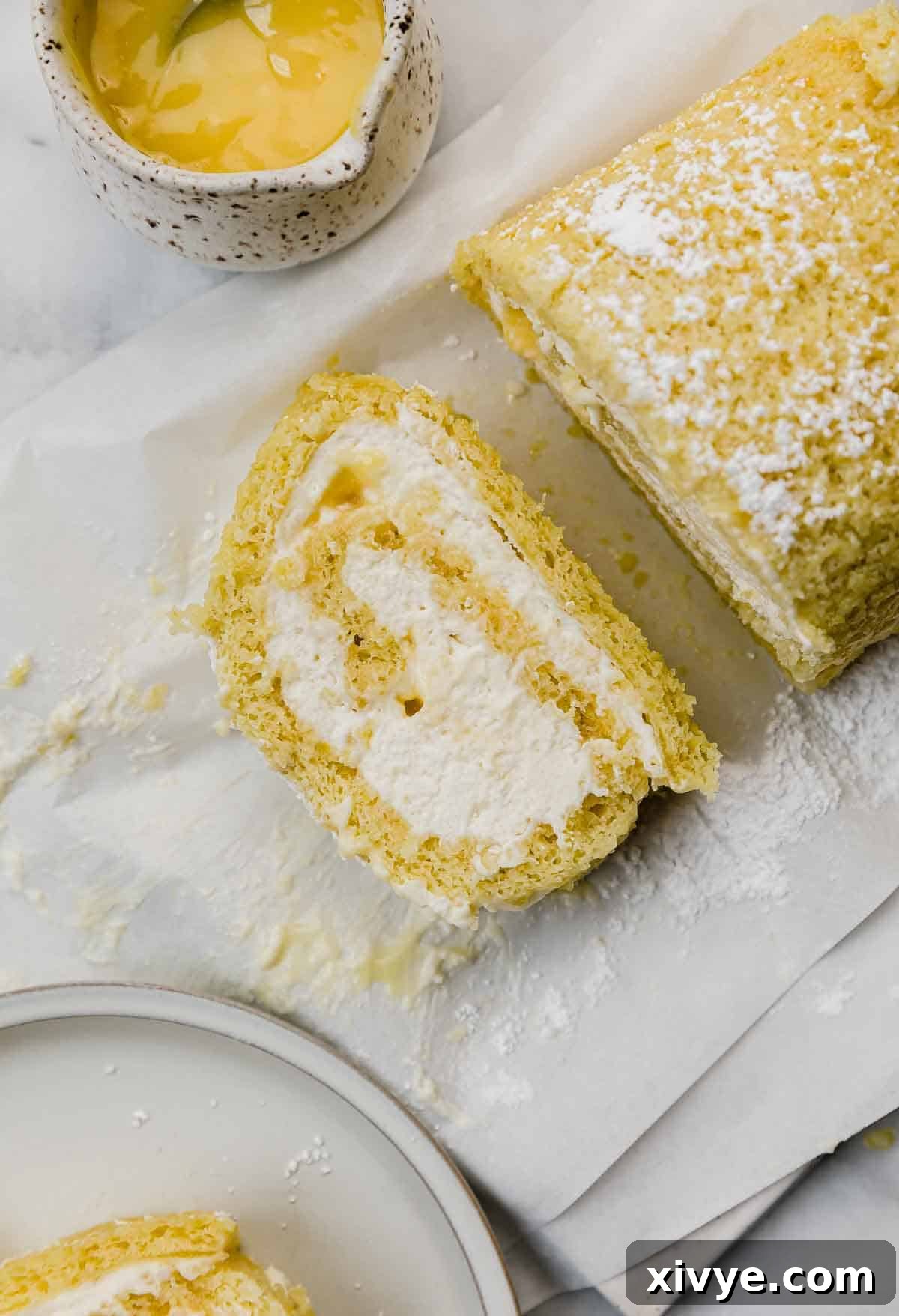 Close-up of a delectable slice of Lemon Swiss Roll, revealing the perfect spiral layers of soft lemon sponge, creamy white filling, and vibrant yellow lemon curd.