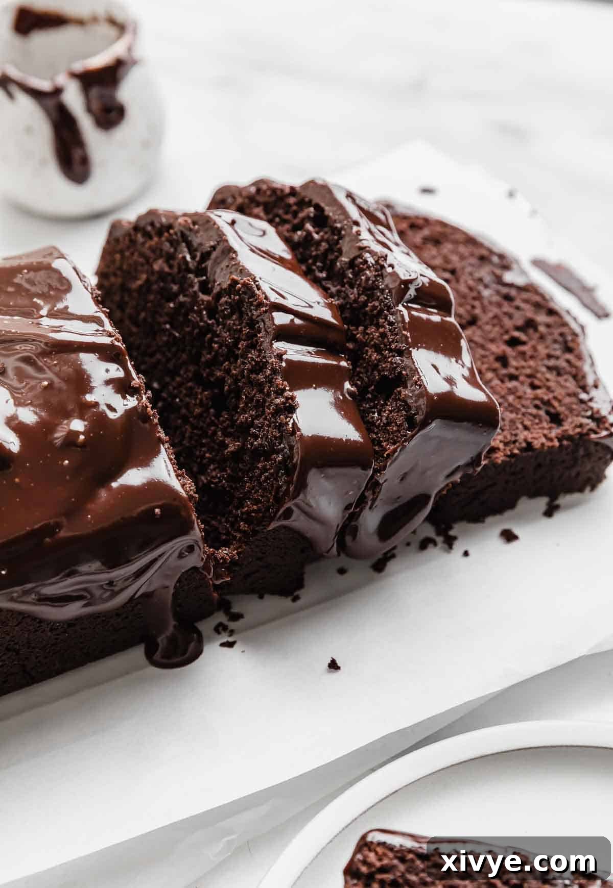 Slices of chocolate glazed Chocolate Pound Cake on a white parchment paper.