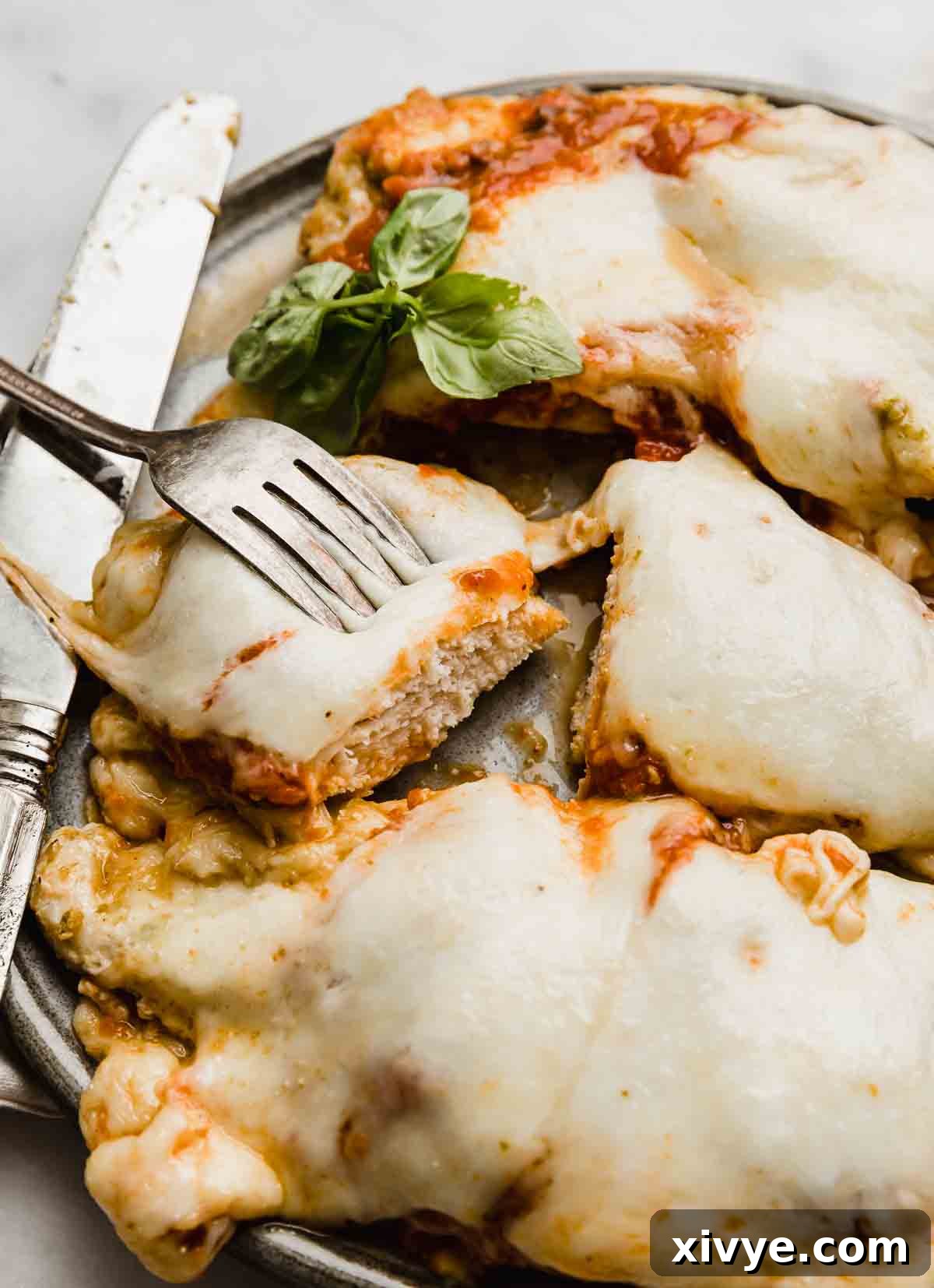 Pesto-Infused Chicken Parmesan 59 A fork holding up a piece of Pesto Chicken Parmesan over a gray plate.