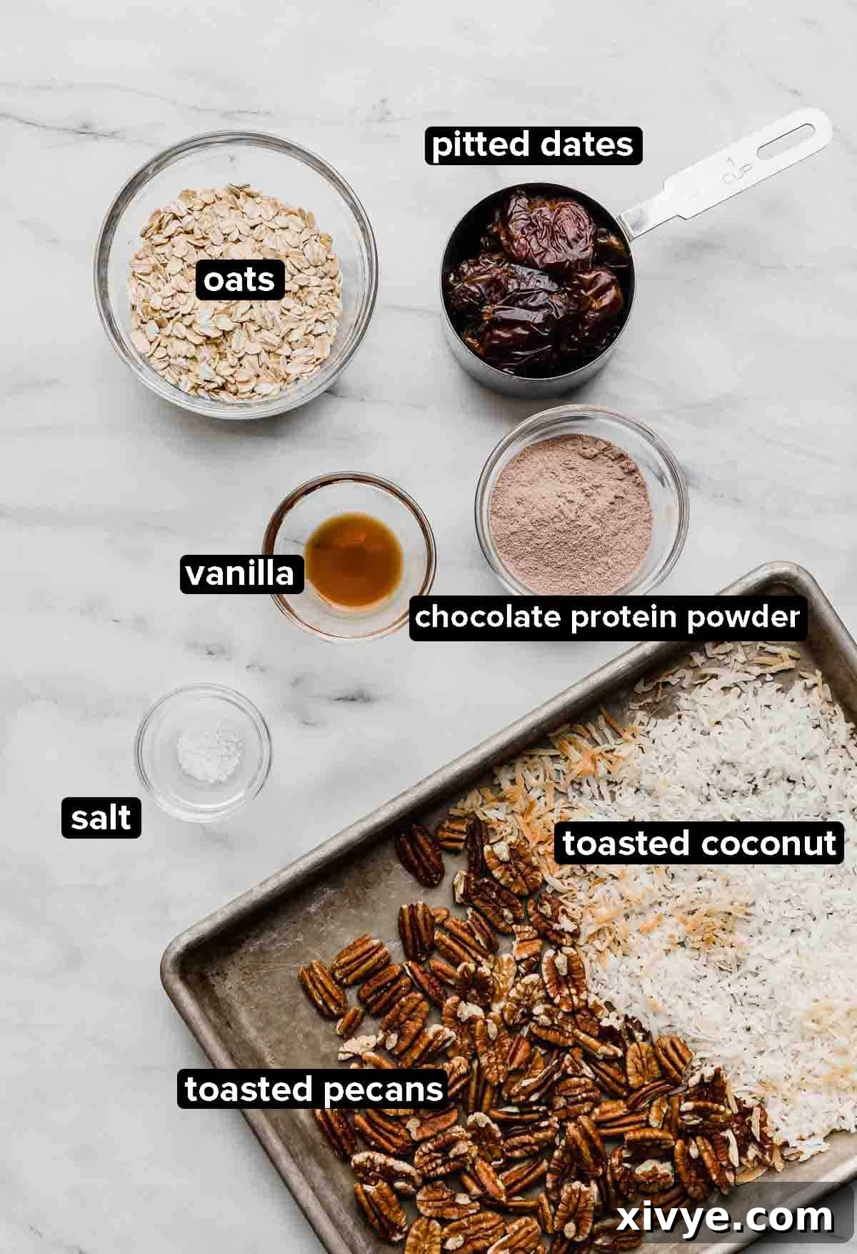 German Chocolate Protein Power Bites 3 German Chocolate protein balls ingredients on a white marble background: pecans, coconut, dates, oats, vanilla, and protein powder.