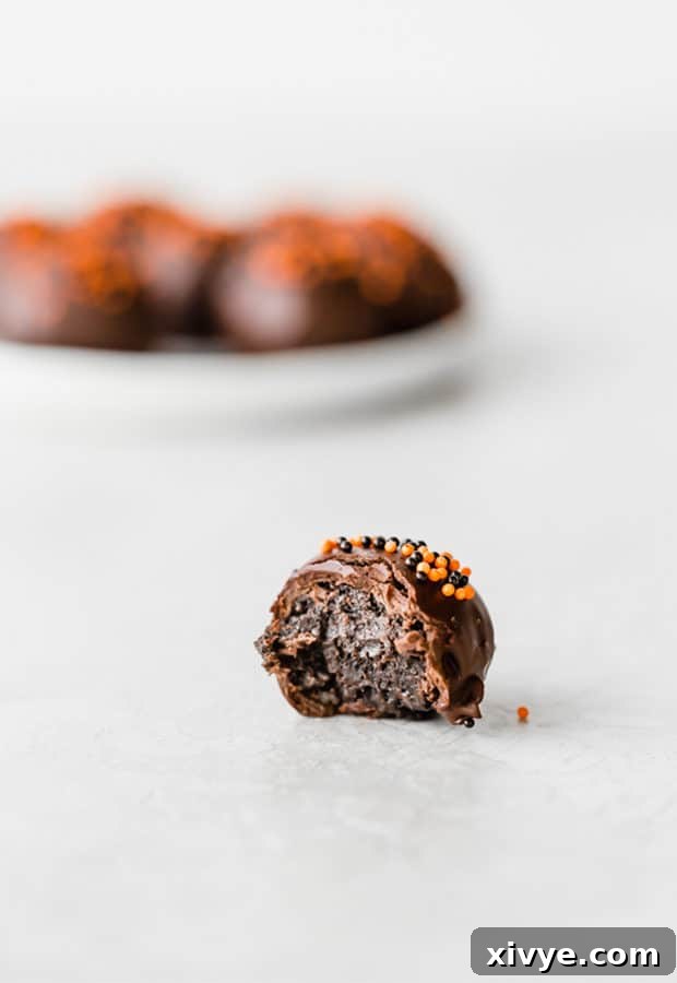 Spooktacular Halloween Oreo Truffles 7 An Oreo ball with a bite taken out of it sitting on a white surface.