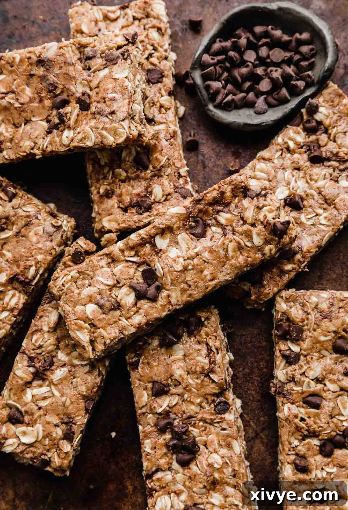 Irresistible Chocolate Peanut Butter Protein Bars 8 An inviting close-up shot of homemade Chocolate Peanut Butter Protein Bars, generously topped with an extra sprinkle of mini chocolate chips, elegantly presented on a rustic brown background, emphasizing their wholesome and appealing qualities.