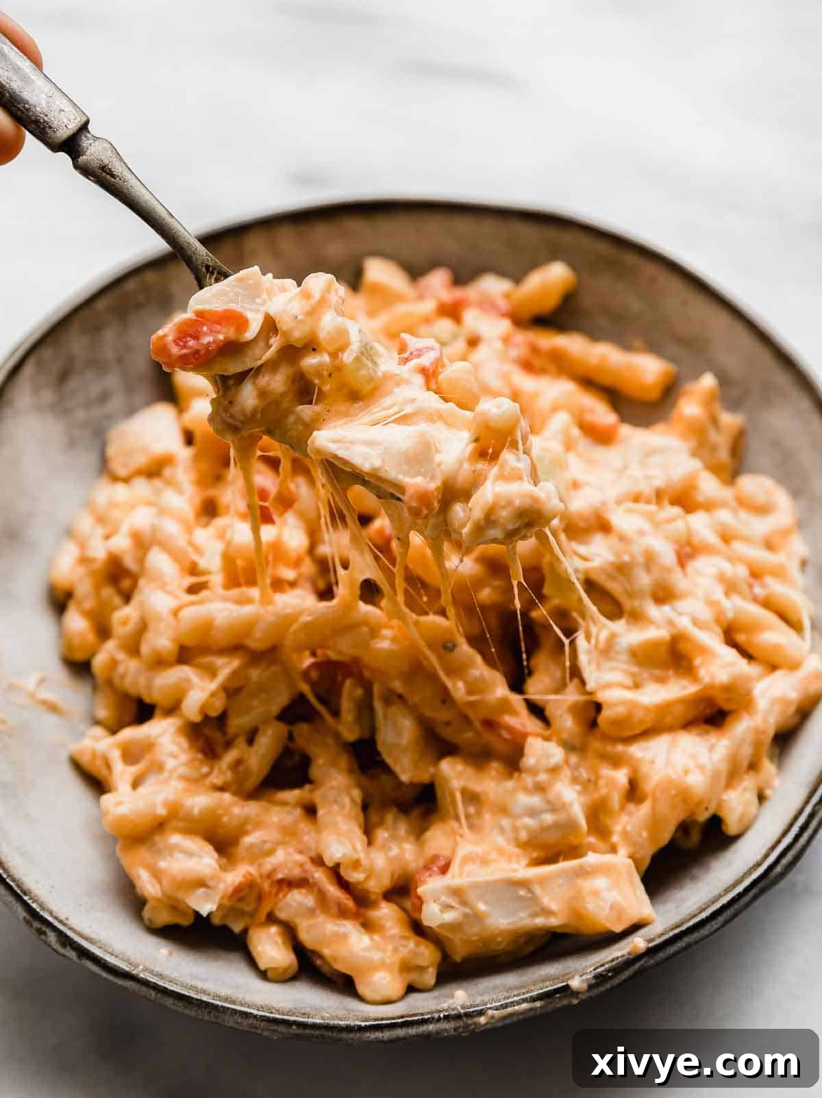 A gray bowl filled with cheesy Buffalo Chicken Pasta and a fork pulling up some of the pasta to show how cheesy it is.