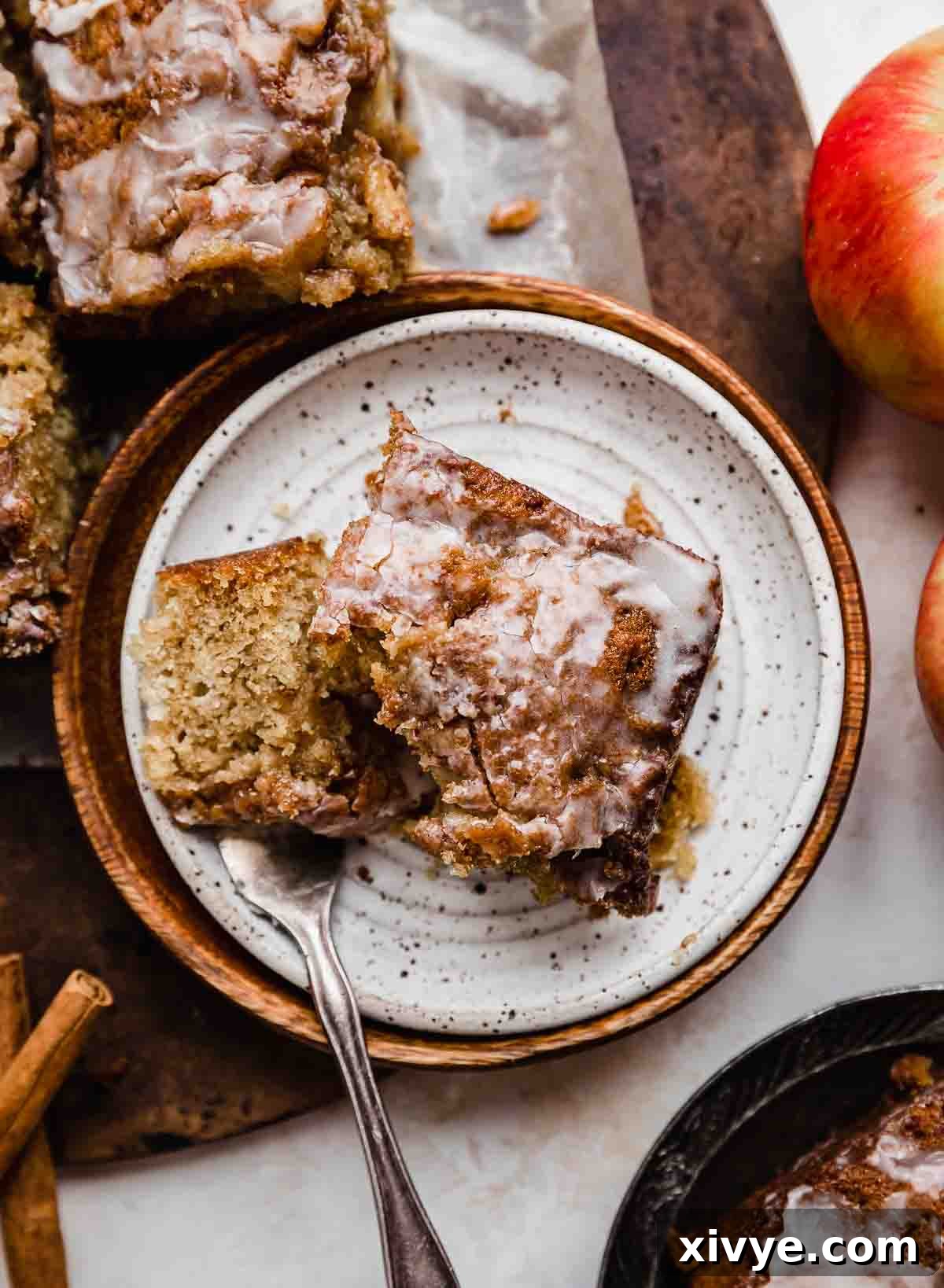 Spiced Apple Fritter Coffee Cake 7 A square slice of iced Apple Fritter Cake on a white plate.