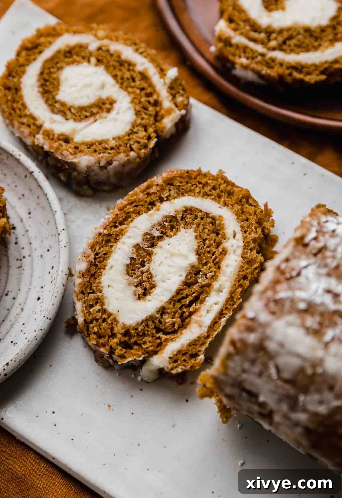Perfect Pumpkin Cream Cheese Roll 2 A slice of pumpkin roll with cream cheese filling on a white plate, garnished with a light dusting of powdered sugar.