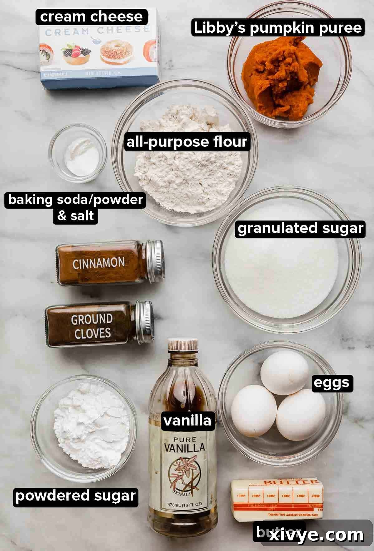 Perfect Pumpkin Cream Cheese Roll 3 Libby's Pumpkin Roll ingredients portioned into glass bowls on a white marble background, showcasing powdered sugar, flour, spices, eggs, pumpkin puree, and cream cheese.