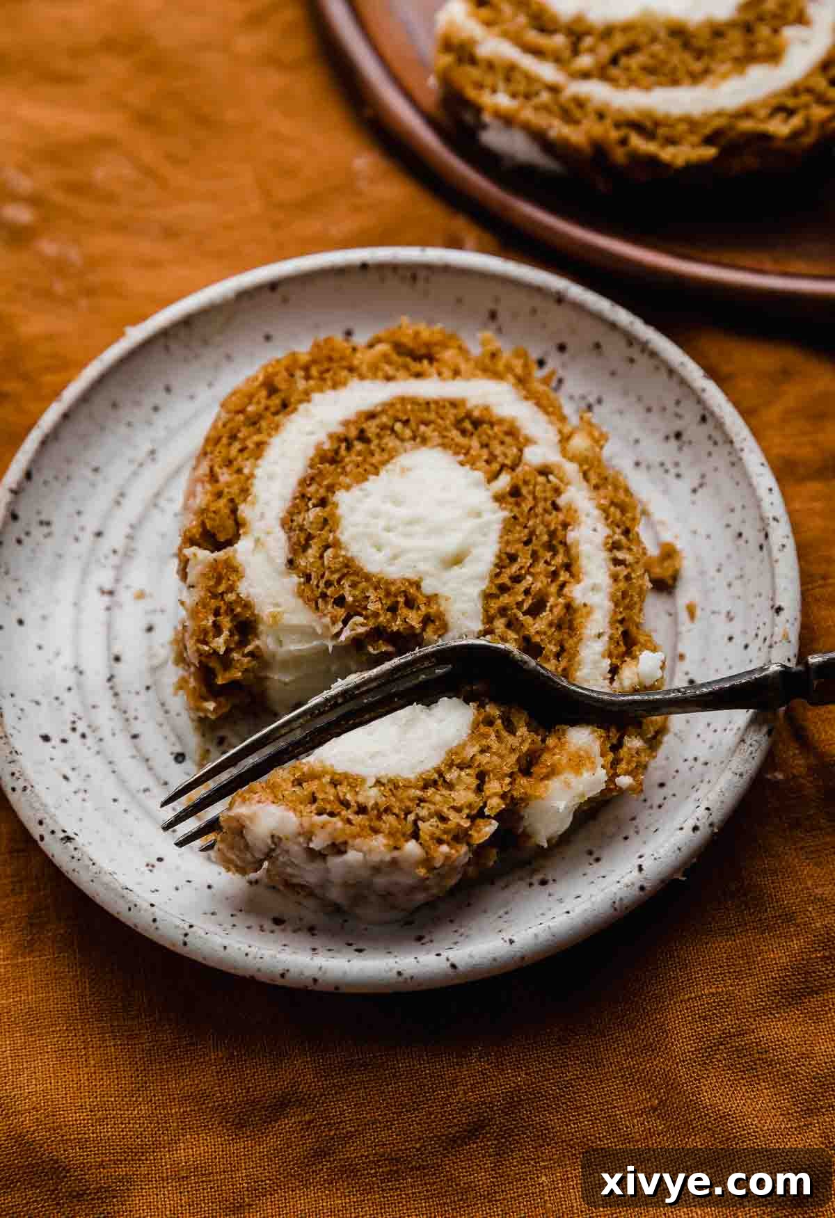 Perfect Pumpkin Cream Cheese Roll 8 A close-up slice of moist pumpkin roll with cream cheese frosting filling, with a fork cutting into the pumpkin cake roll, showing its soft texture.