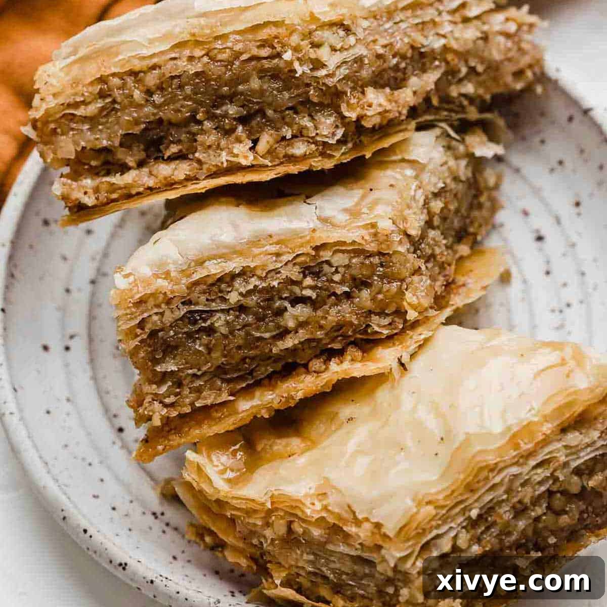 Honeyed Layers of Greece 2 Three Greek Baklava pastries on a white plate, showcasing their golden layers and honey glaze.