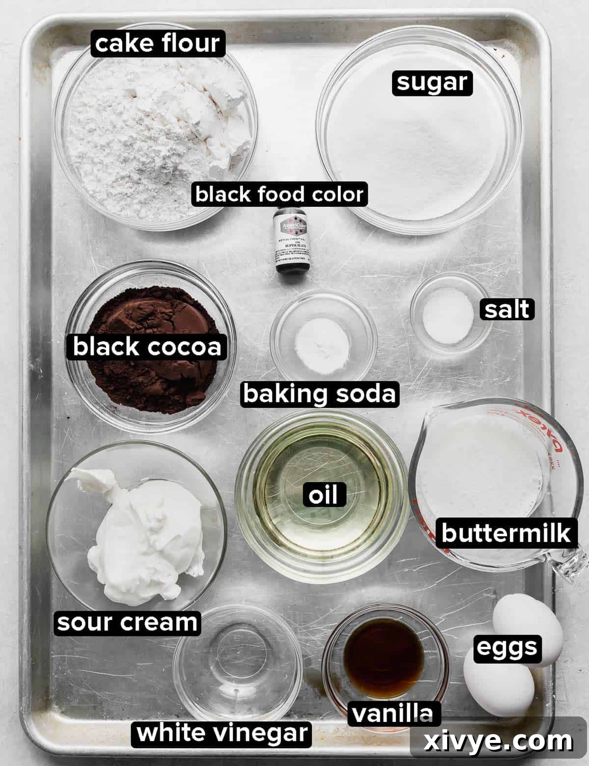 Individual portions of black velvet cake ingredients neatly arranged in glass bowls on a shining silver baking sheet.