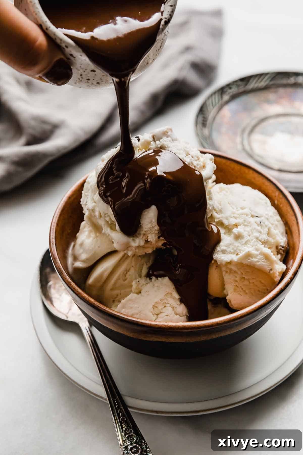Magic Shell with coconut oil being poured overtop scoops of vanilla ice cream.