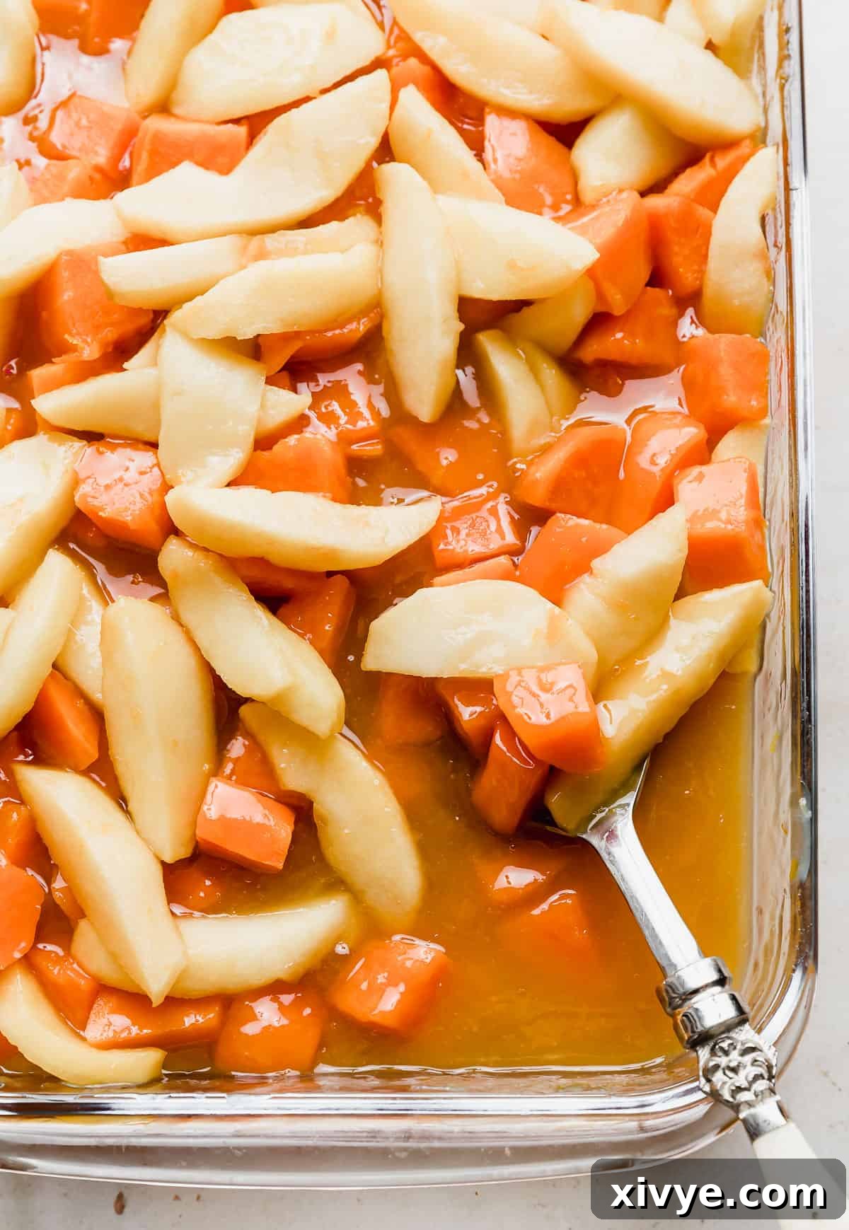 Vibrantly orange candied yams with apple slices glistening in a glass baking dish, ready to be served.