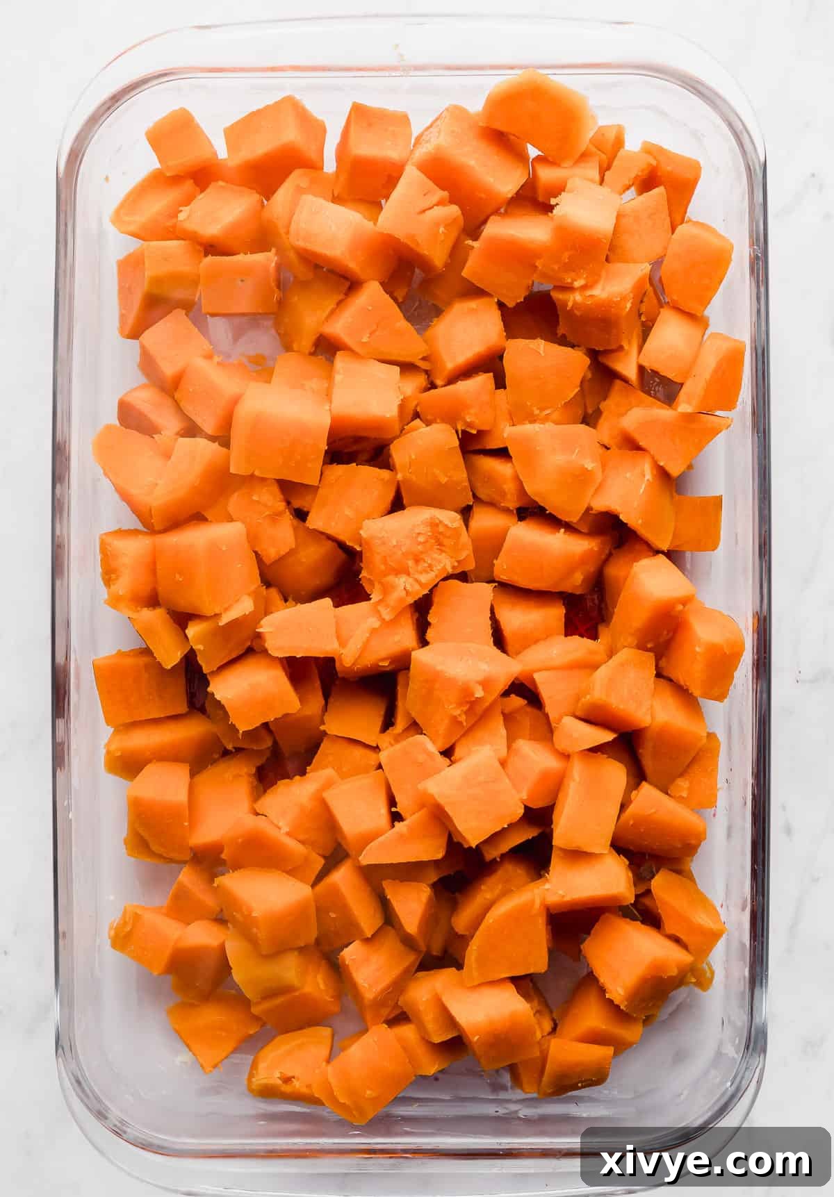 Cubed sweet potatoes, perfectly cooked and arranged in a clear glass casserole dish, ready for the next layer.