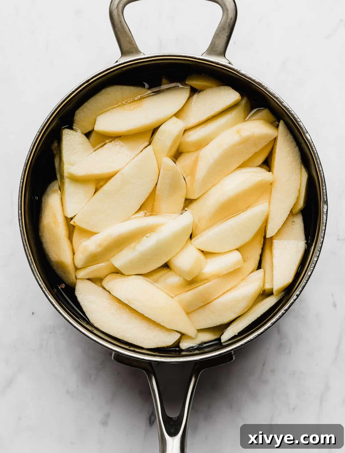 Peeled and uniformly sliced apples simmering gently in a saucepan filled with water.