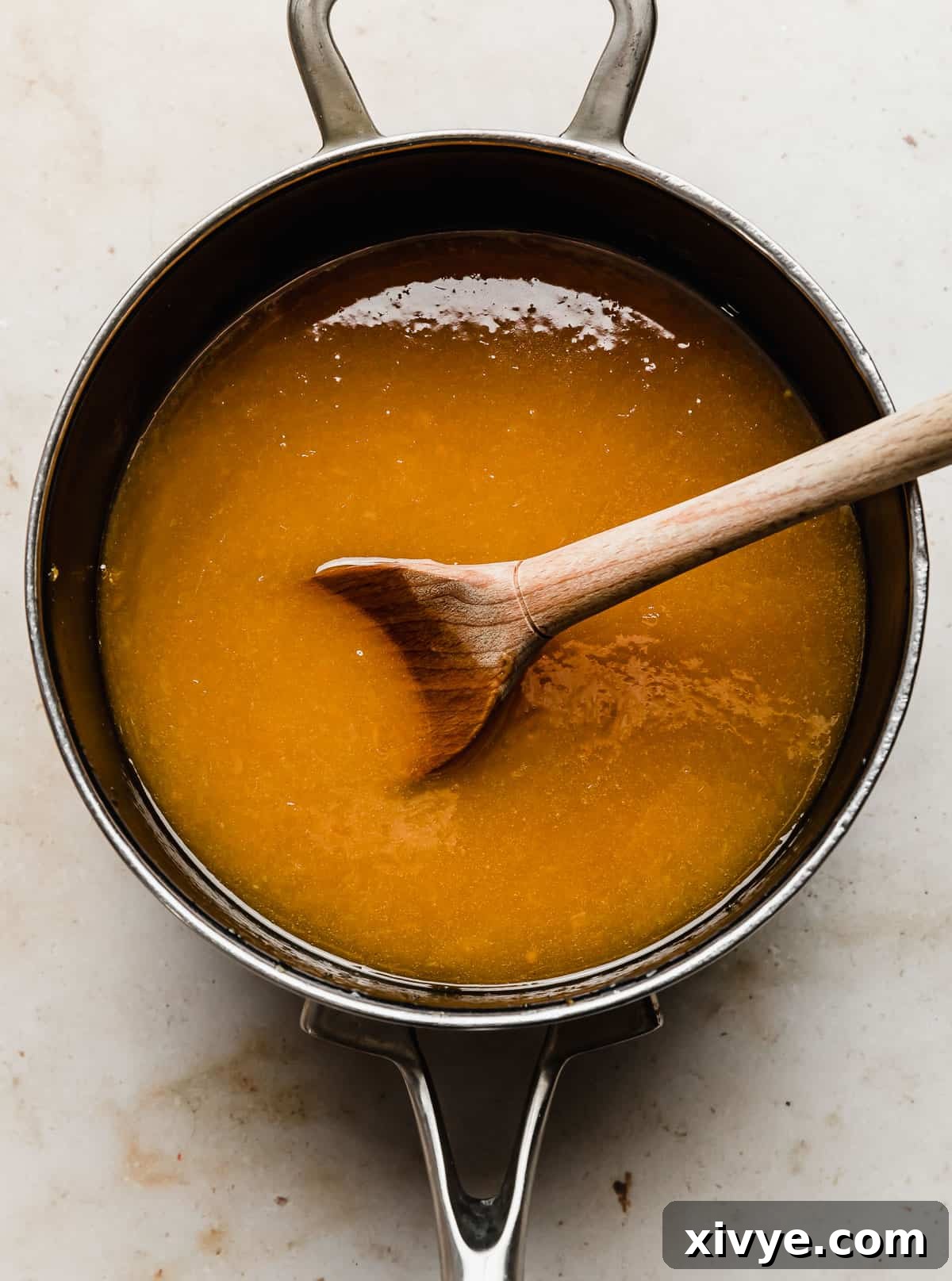 A deep, inviting orange-colored orange juice candied yams sauce, showcasing its perfectly thick, syrupy texture in a saucepan.