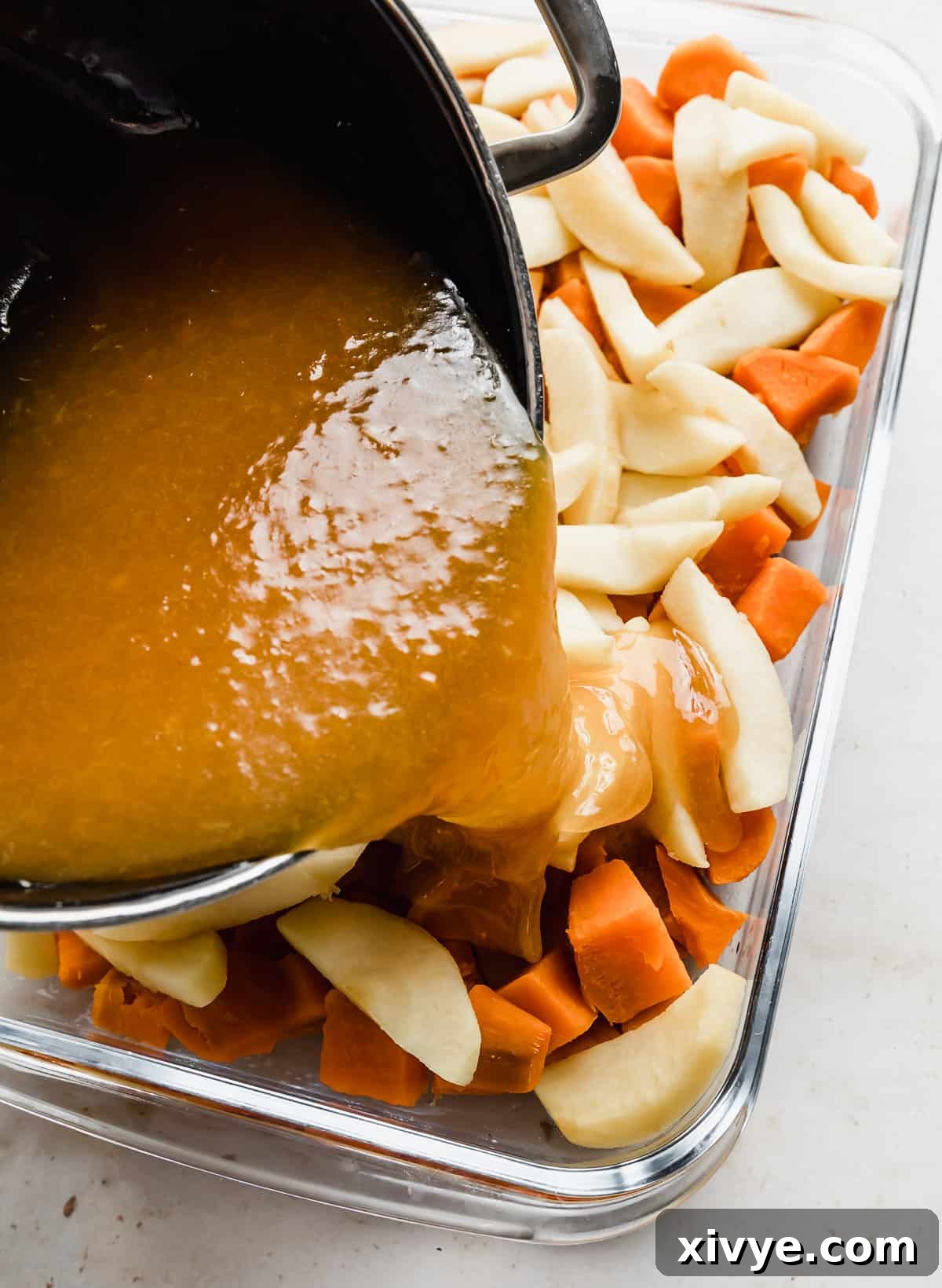 A luscious orange juice sauce being generously poured over a bed of tender cubed sweet potatoes and delicate sliced apples in a casserole dish, preparing it for baking.