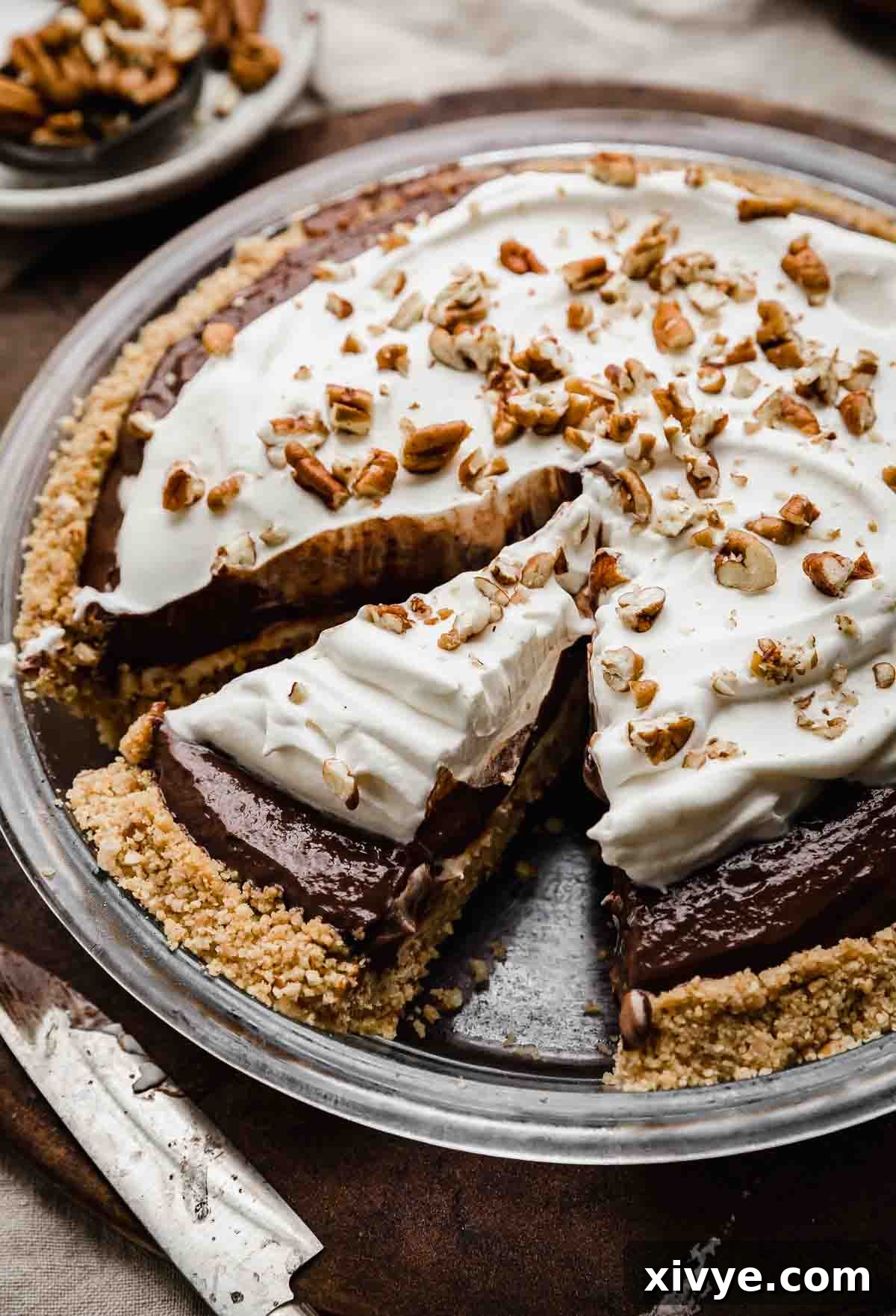 A Possum Pie topped with whipped cream and chopped pecans, on a brown background.