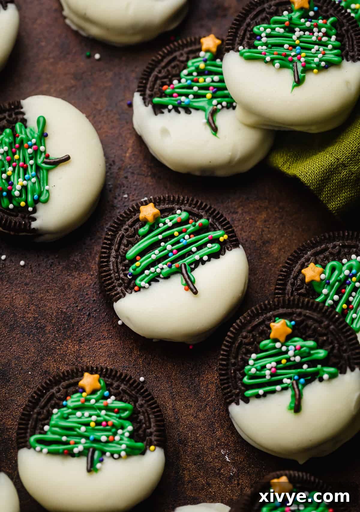 Christmas Tree Oreos on a brown background, an Oreo half dipped in white chocolate with a green Christmas tree piped on the Oreos and topped with nonpareil sprinkles.