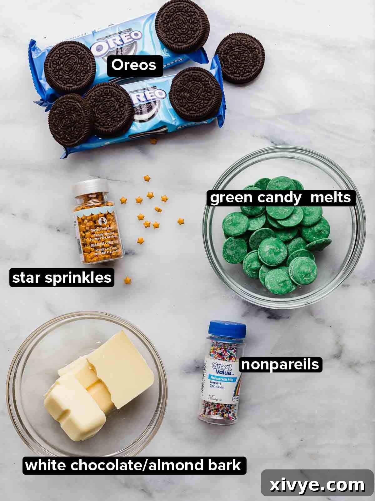 Christmas Tree Oreos ingredients on a white marble background: Oreos, green candy melts, white chocolate, nonpareil sprinkles, and star sprinkles.