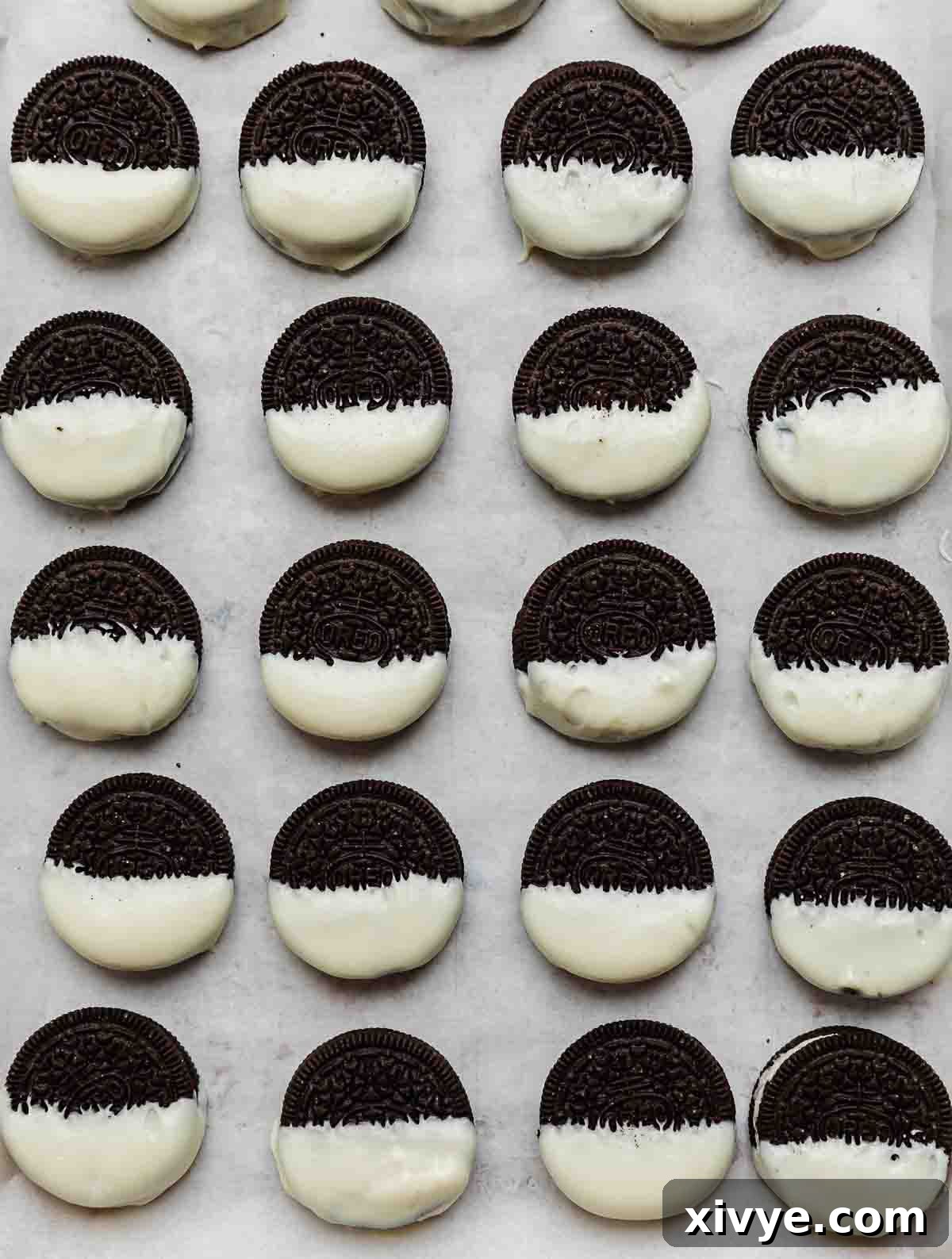 Half dipped white chocolate Oreos on a parchment paper lined baking sheet.