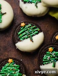 Christmas Tree Oreos on a brown background, an Oreo half dipped in white chocolate with a green Christmas tree piped on the Oreos and topped with nonpareil sprinkles.