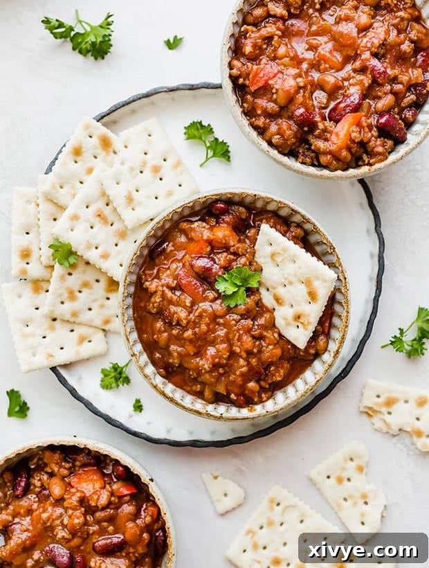 Three bowls of rich, sweet and spicy chili garnished with saltine crackers, ready to be served.