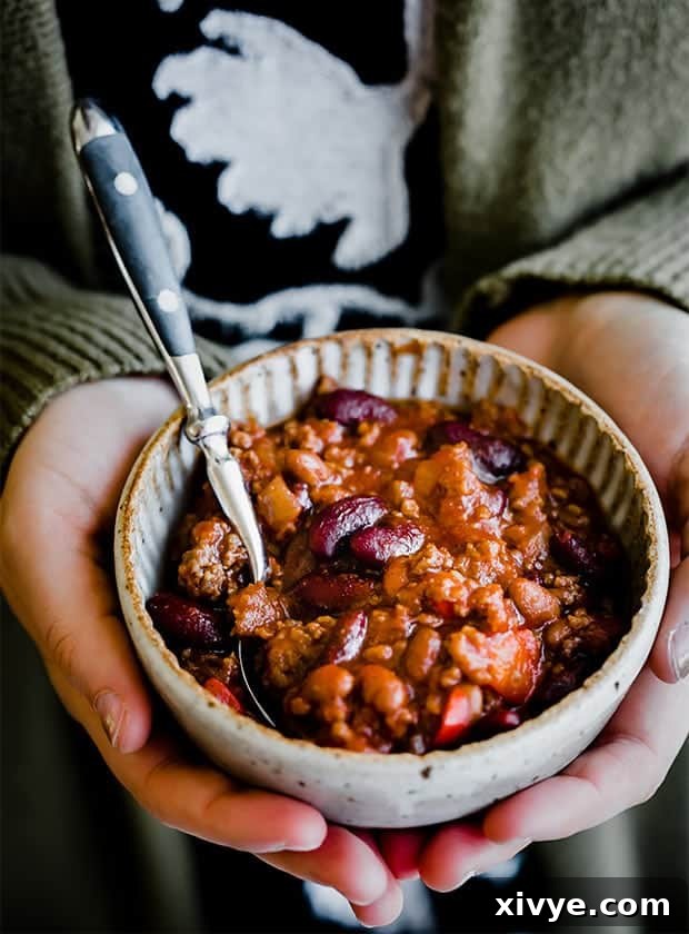 A bowl of sweet and spicy chili being held in a woman's hands, showcasing its inviting texture.
