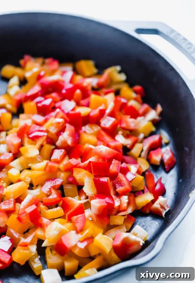 Diced yellow and red bell peppers with sweet onions sautéing in a black skillet, the aromatic start to the sweet and spicy chili.