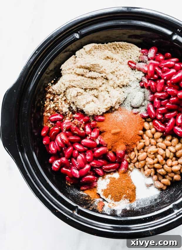 An overhead photo of a black slow cooker brimming with all the ingredients for sweet and spicy chili, ready to simmer.