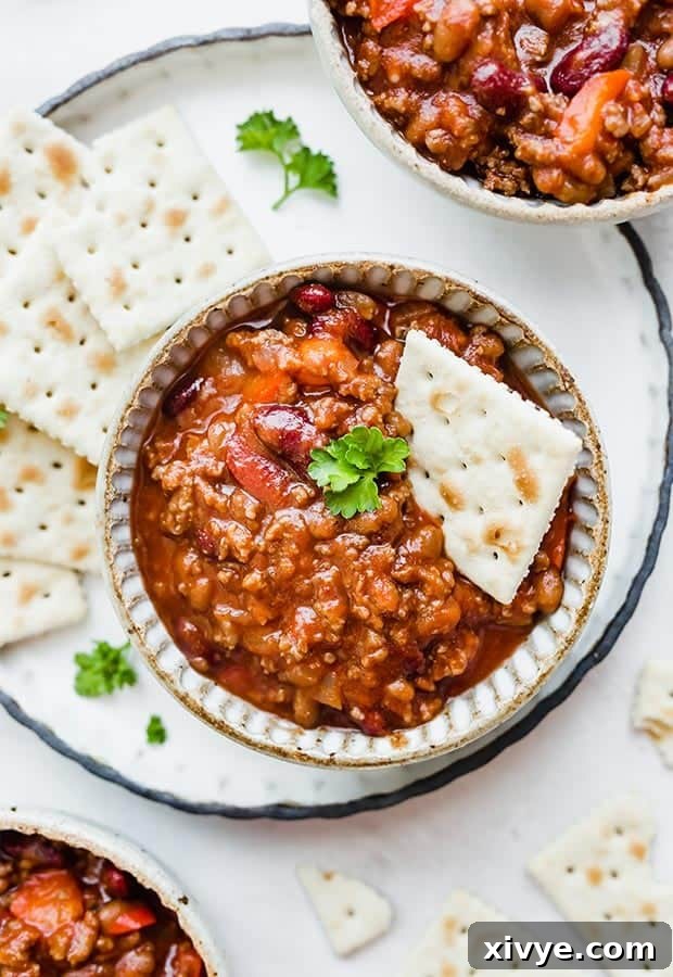 Three bowls of sweet and spicy chili, generously garnished with saltine crackers, ready for a comforting meal.