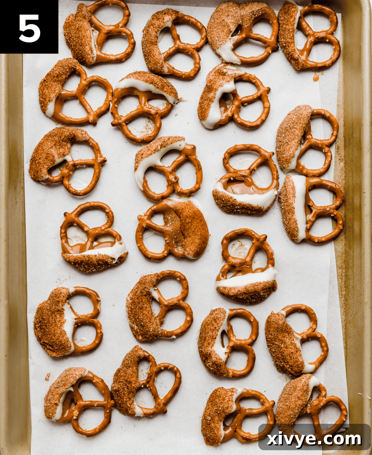 Caramel coated snickerdoodle pretzels resting on a white parchment paper, setting.