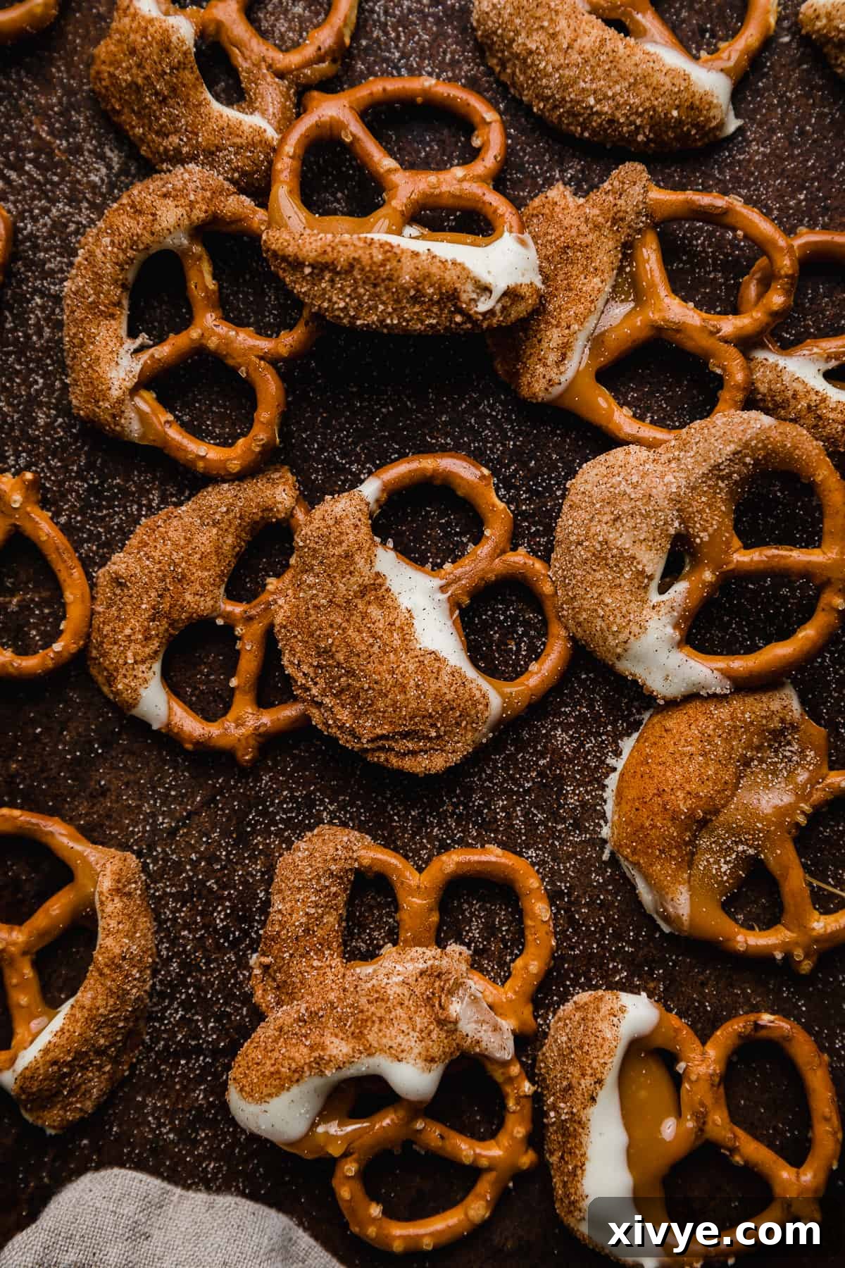 Pretzels coated in caramel, then white chocolate and a cinnamon sugar mixture on a brown background, stacked invitingly.