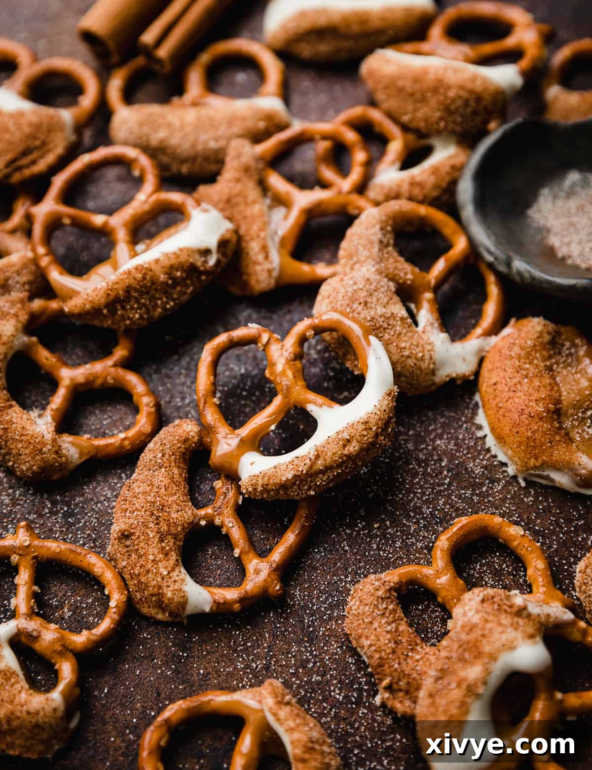 Snickerdoodle pretzels (half dipped pretzels in caramel, white chocolate, and cinnamon sugar) on a brown background, beautifully arranged.