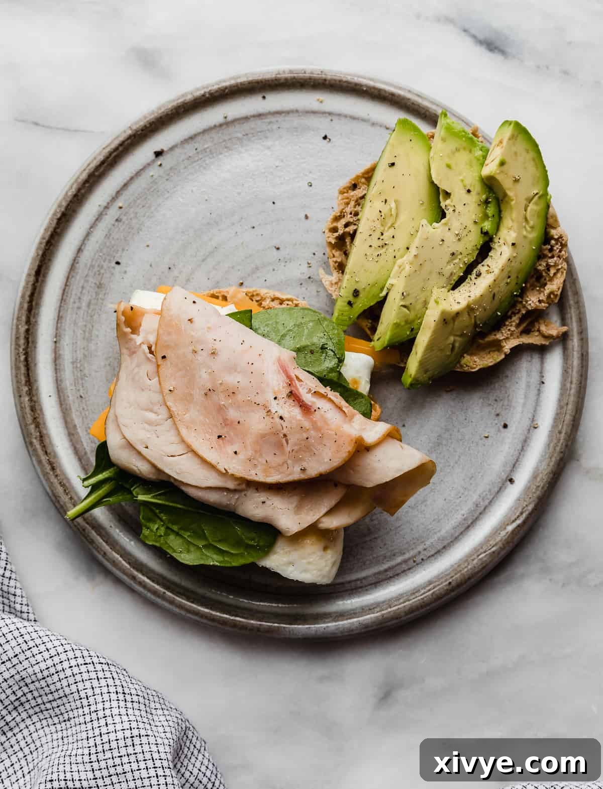 A close-up view of an English muffin layered with creamy avocado, fresh spinach, a perfectly cooked egg, and savory turkey meat.