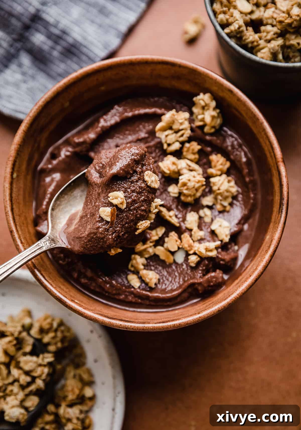 Decadent Chocolate Acai Bliss 5 A spoon scooping up frozen chocolate açaí smoothie in a brown bowl that's topped with granola.